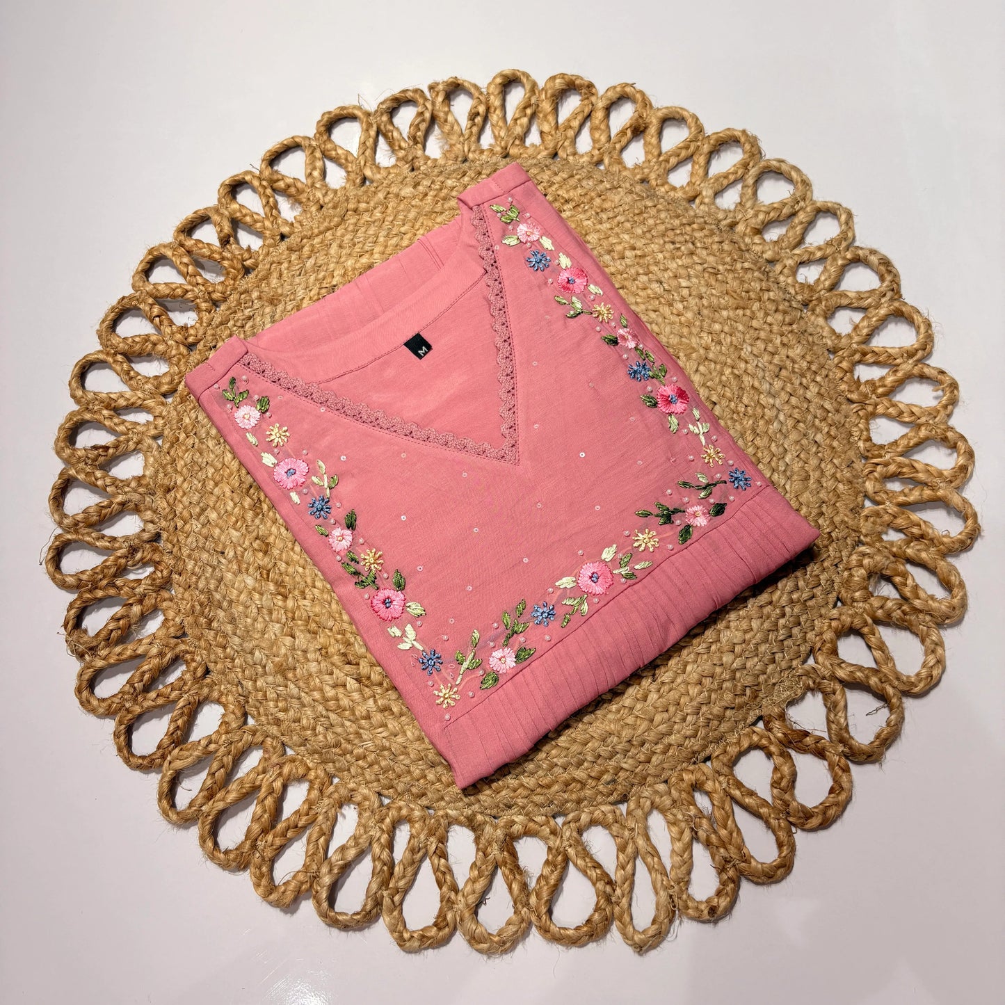 Pink embroidered fabric on a woven placemat with a plain background