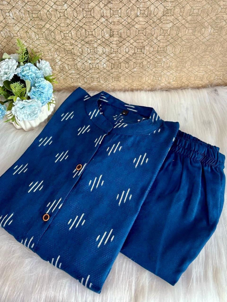 Blue pants with white patterns on a light wooden surface with a woven mat and flowers in the background.
