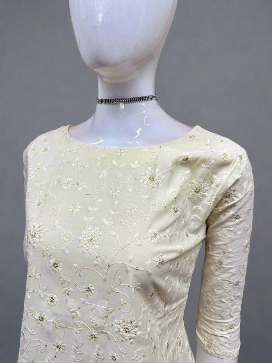 White embroidered dress on a mannequin against a geometric patterned wall.