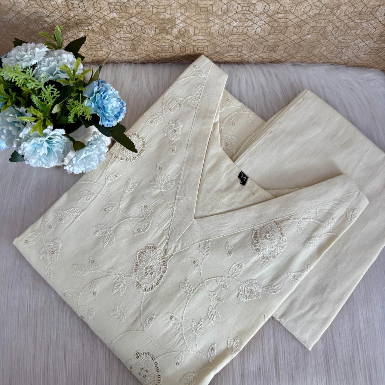Beige embroidered pajama set on a bed with a vase of flowers.