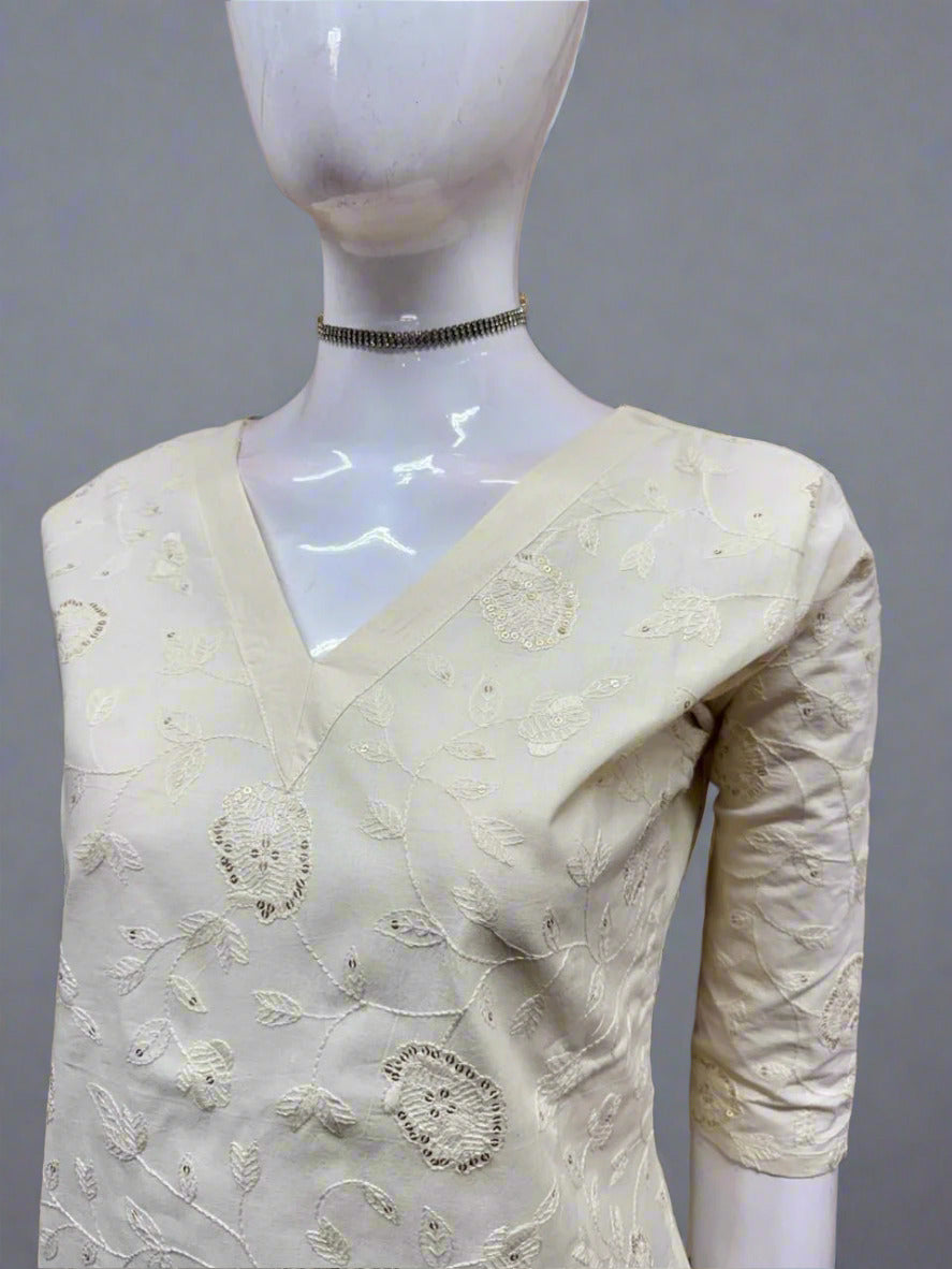Mannequin wearing a cream saree with intricate patterns against a tiled wall.