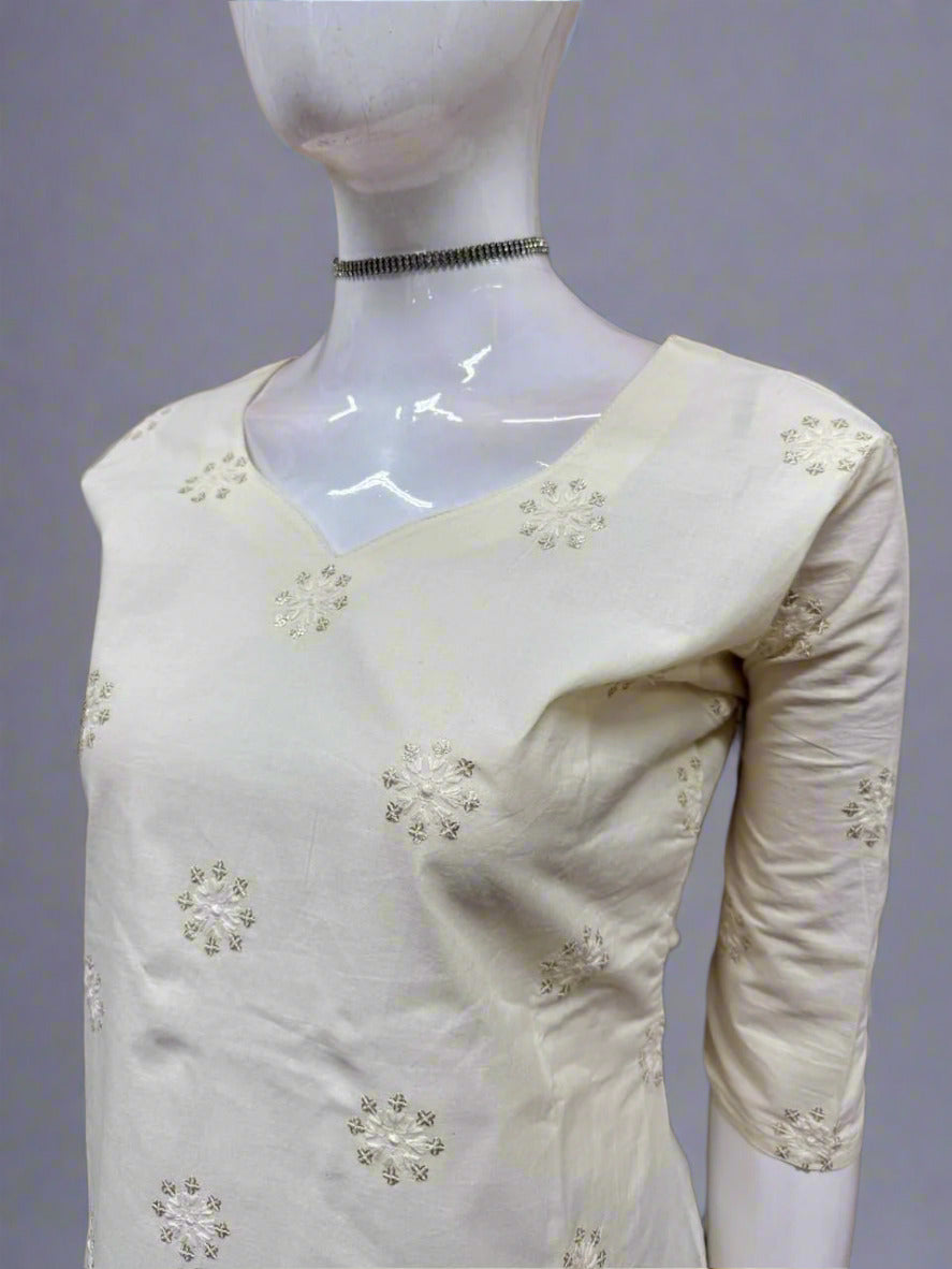 White dress with floral embellishments on a mannequin against a geometric-patterned wall.