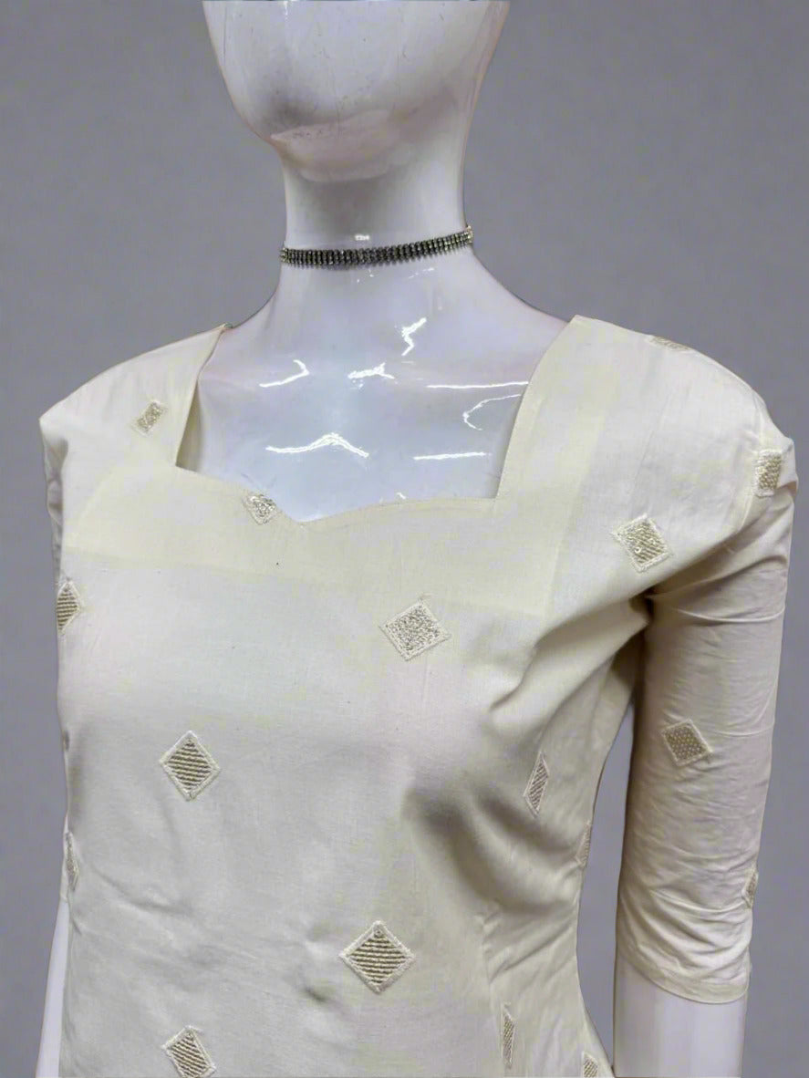 White saree with gold patterns on a mannequin against a geometric patterned wall.