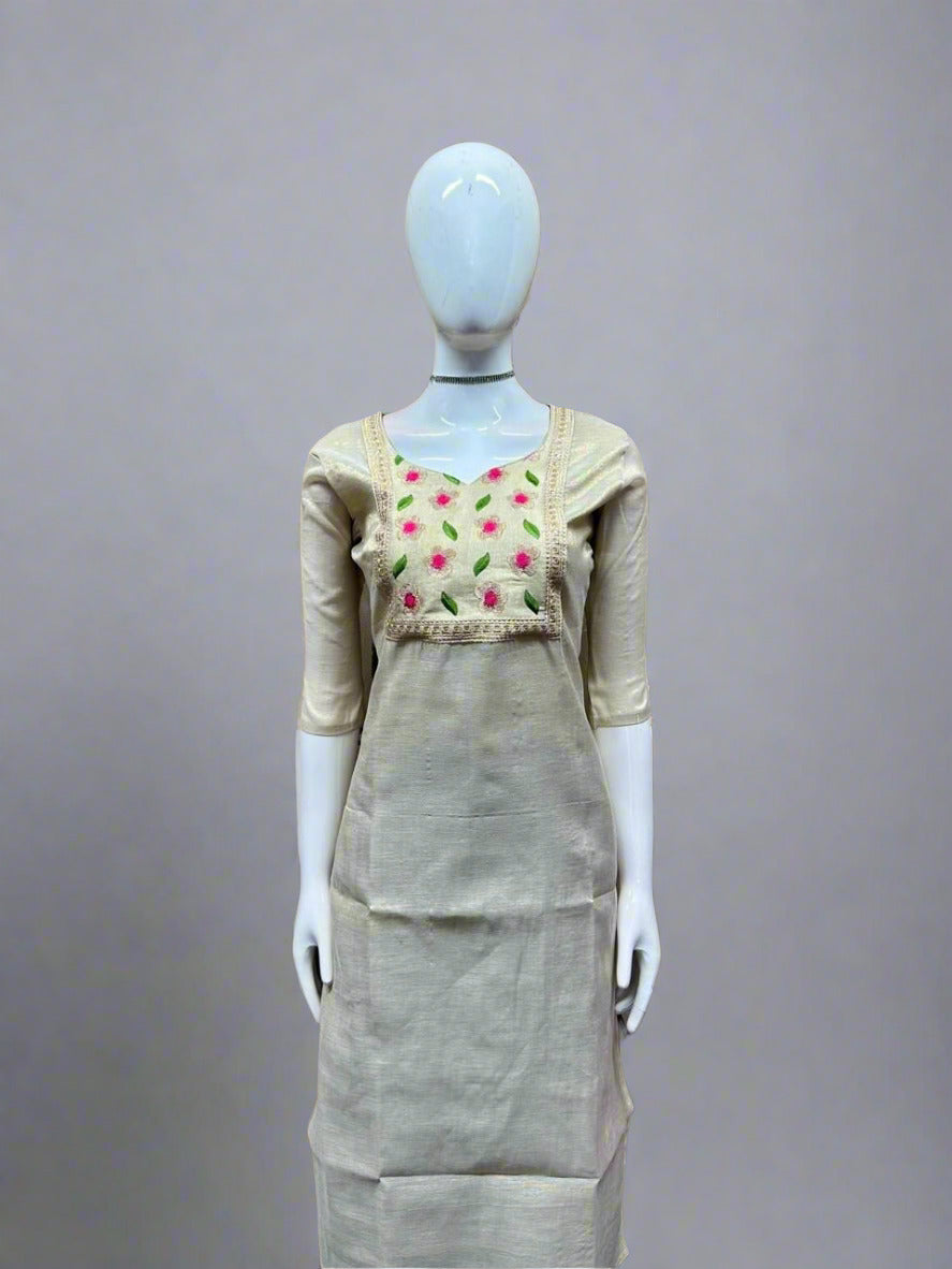 Mannequin wearing a beige dress with floral embroidery against a geometric patterned wall.
