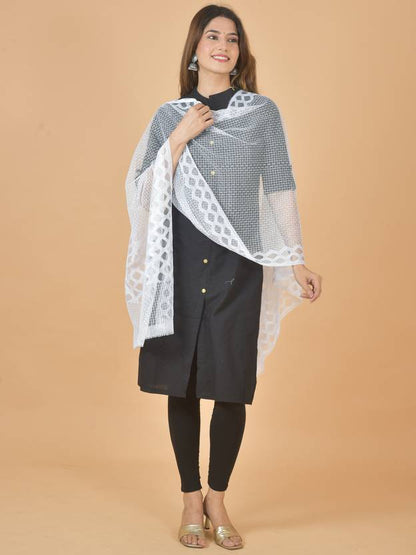 Woman wearing a black kurta with a white lace dupatta against a beige background