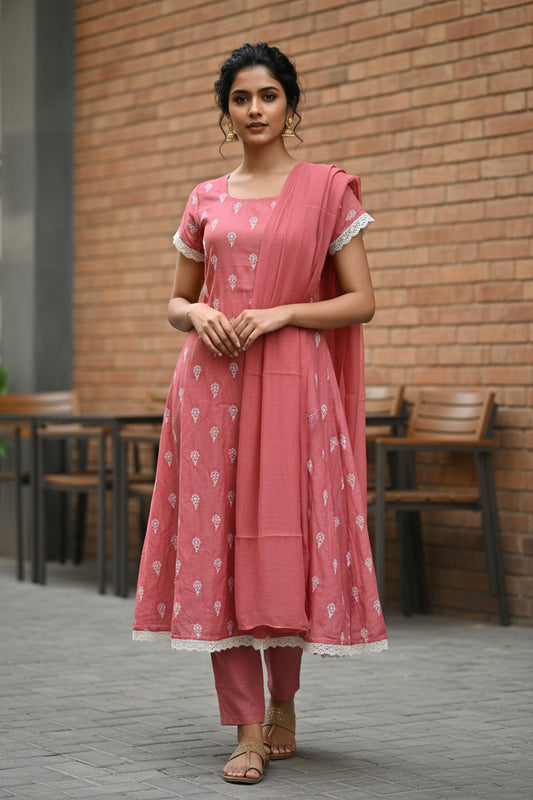 Woman in a pink traditional outfit standing in front of a brick wall.