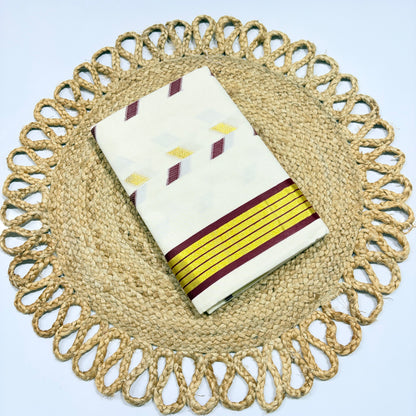 Off-white Kerala cotton saree with multicolour diamond butta motifs and yellow-maroon stripe border, neatly folded on a jute woven placemat – perfect for Onam, festivals and office wear