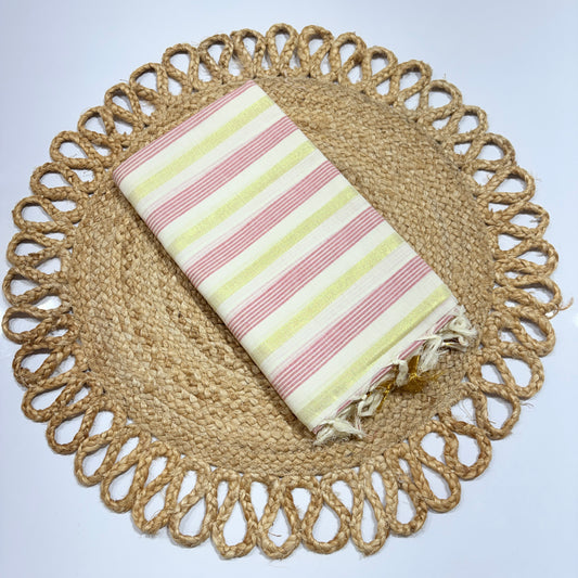 Kerala Cotton Saree Off-White with Pink & Yellow 6-Line Zari Stripe Weave and Gold Tassel Pallu – neatly folded on a jute woven placemat, lightweight Onam and festival saree by RAE Trends