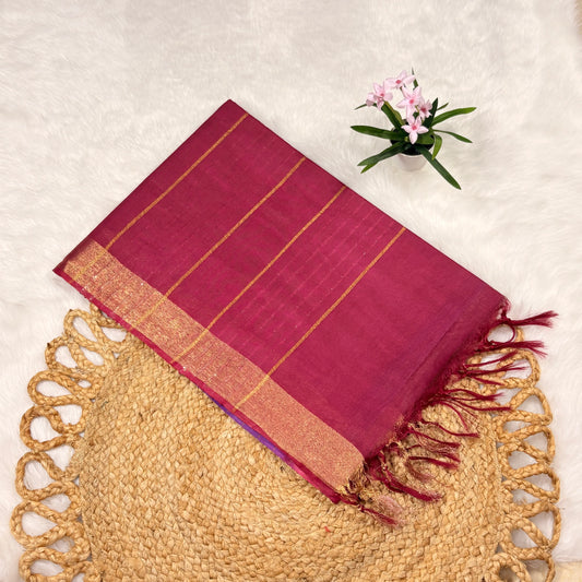 Red saree with gold border on a textured surface with a small plant.