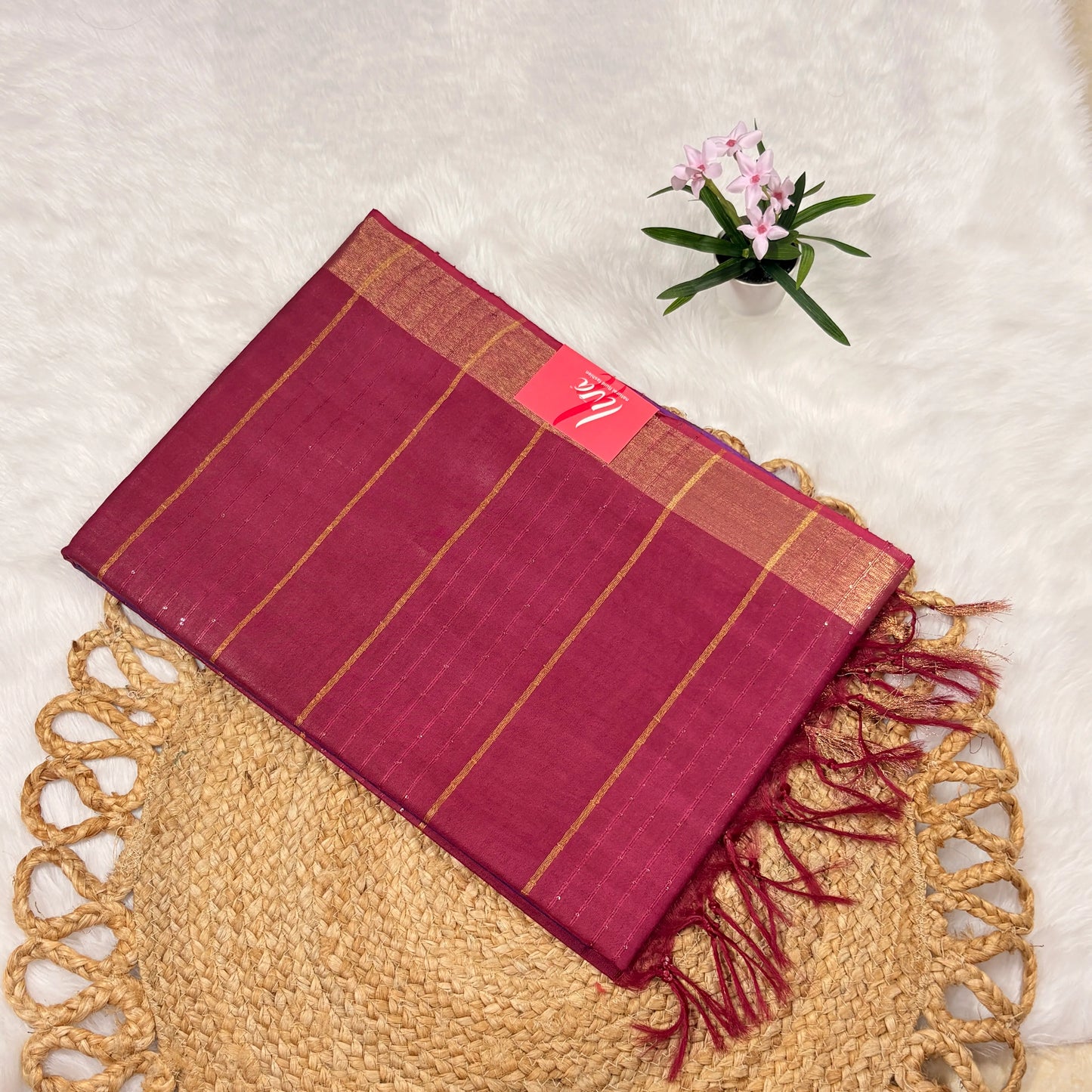 Wine Bapta Tussar saree with woven gold zari lines, subtle sequin accents, tasselled pallu, and matching blouse piece, folded on a natural jute mat