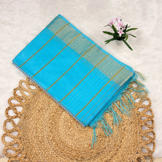 Aqua blue Bapta Tussar silk saree with woven zari lines, subtle sequin accents, tasselled pallu, and matching blouse piece, folded on a natural mat