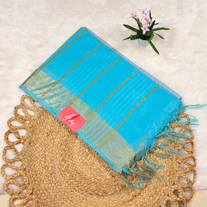 Turquoise scarf with gold stripes and tassels on a textured surface with a plant in the corner.