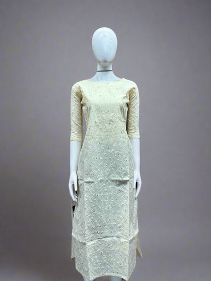 Mannequin wearing a light-colored dress against a geometric patterned wall.