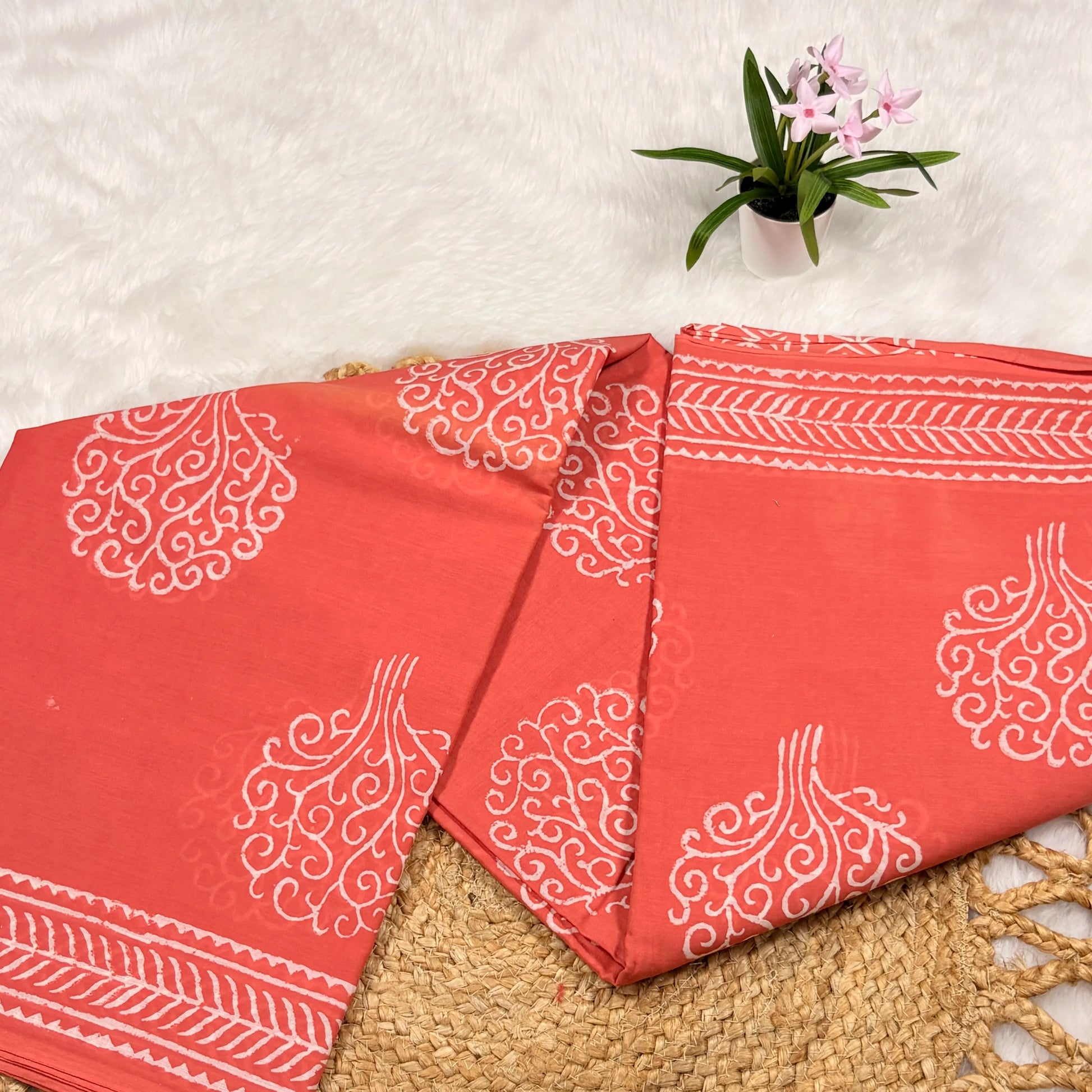 Red fabric with white patterns on a textured surface with a small plant in the background