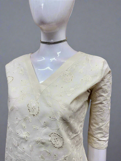 Mannequin wearing a cream saree with intricate patterns against a tiled wall.