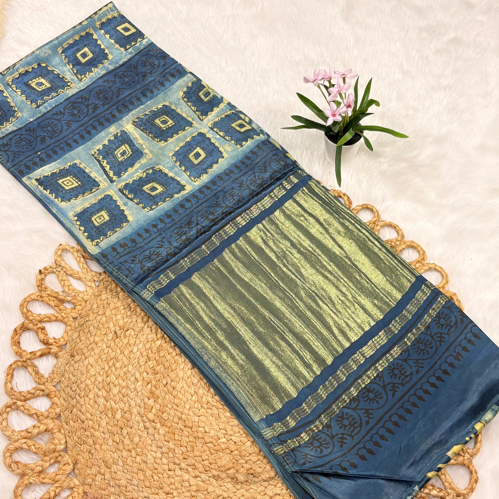 Blue and green patterned fabric with a woven mat and small plant on a light background