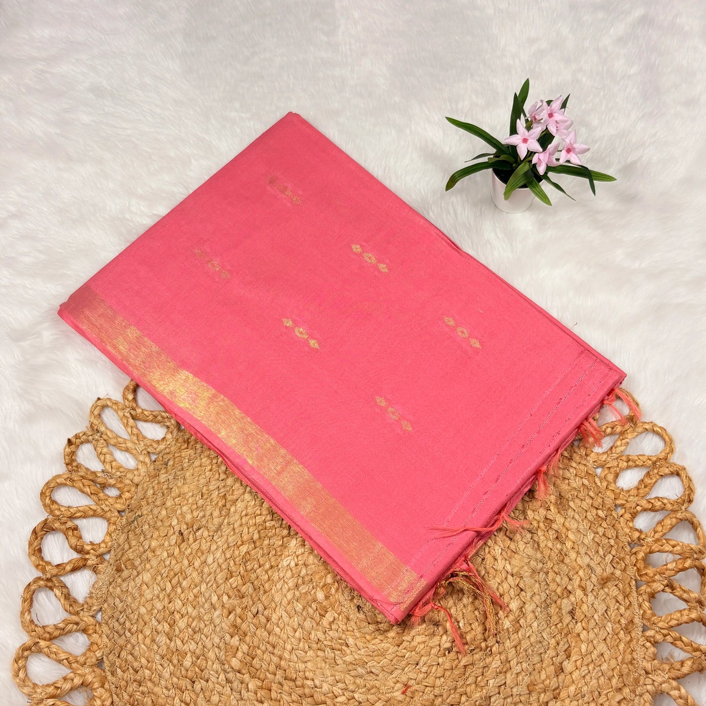 Rose‑pink Liva saree with scattered zari buti motifs, linear jari pallu, tasselled edge, and matching blouse piece, folded on a natural mat.