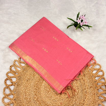 Rose‑pink Liva saree with scattered zari buti motifs, linear jari pallu, tasselled edge, and matching blouse piece, folded on a natural mat.