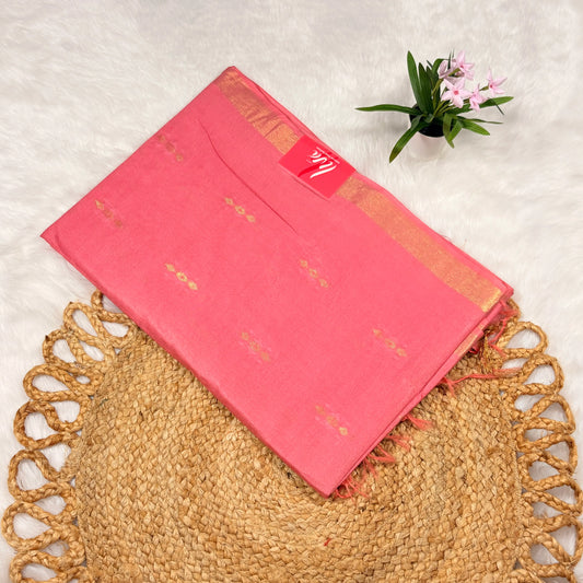 Rose‑pink Liva saree with scattered zari buti motifs, linear jari pallu, tasselled edge, and matching blouse piece, folded on a natural mat.