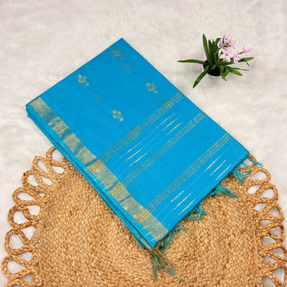 Blue saree with green border on a textured surface with a plant