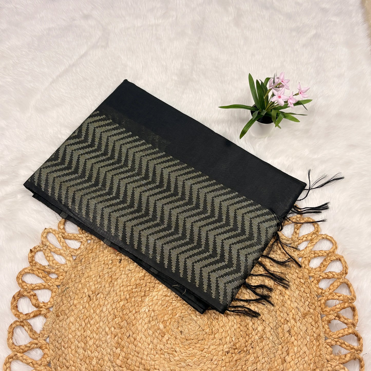 Black and gray patterned scarf with fringes on a textured surface with a plant.