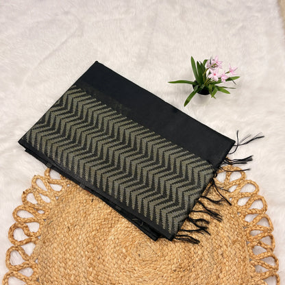 Black and gray patterned scarf with fringes on a textured surface with a plant.