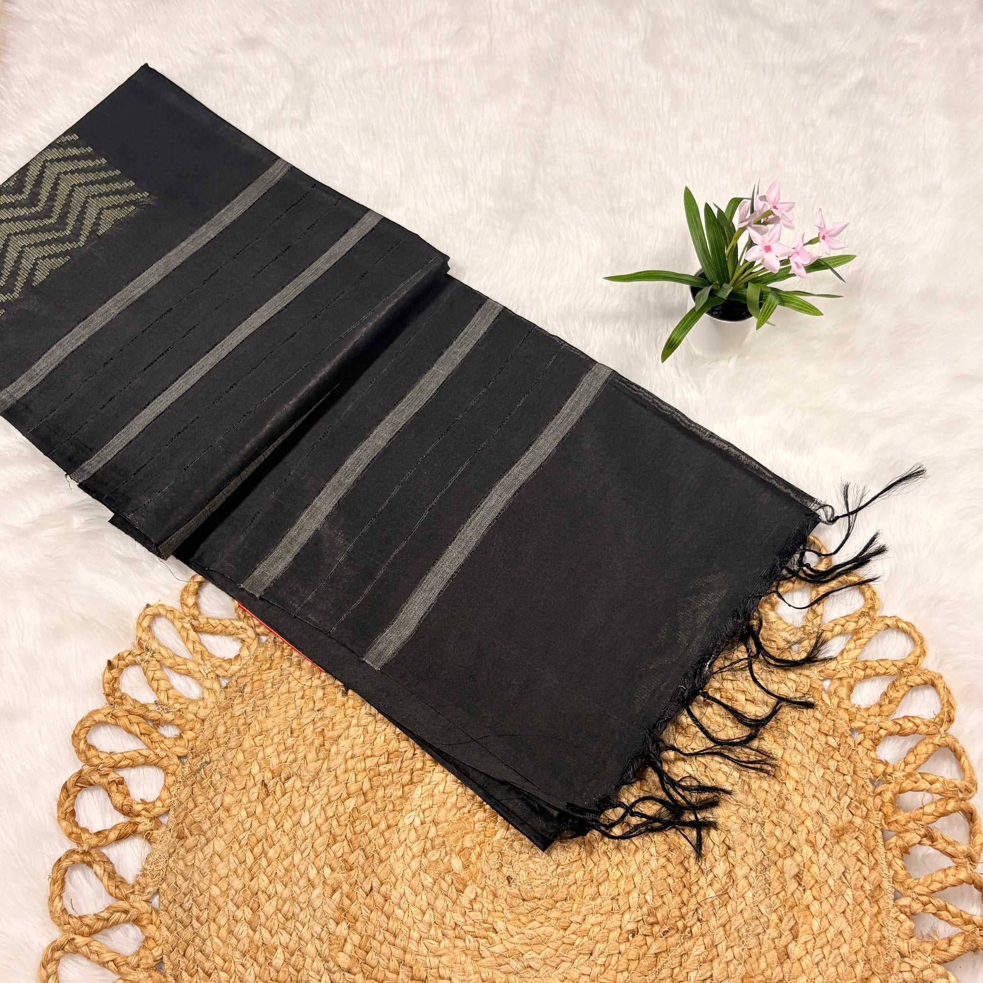 Black scarf with gray stripes on a textured surface with a plant