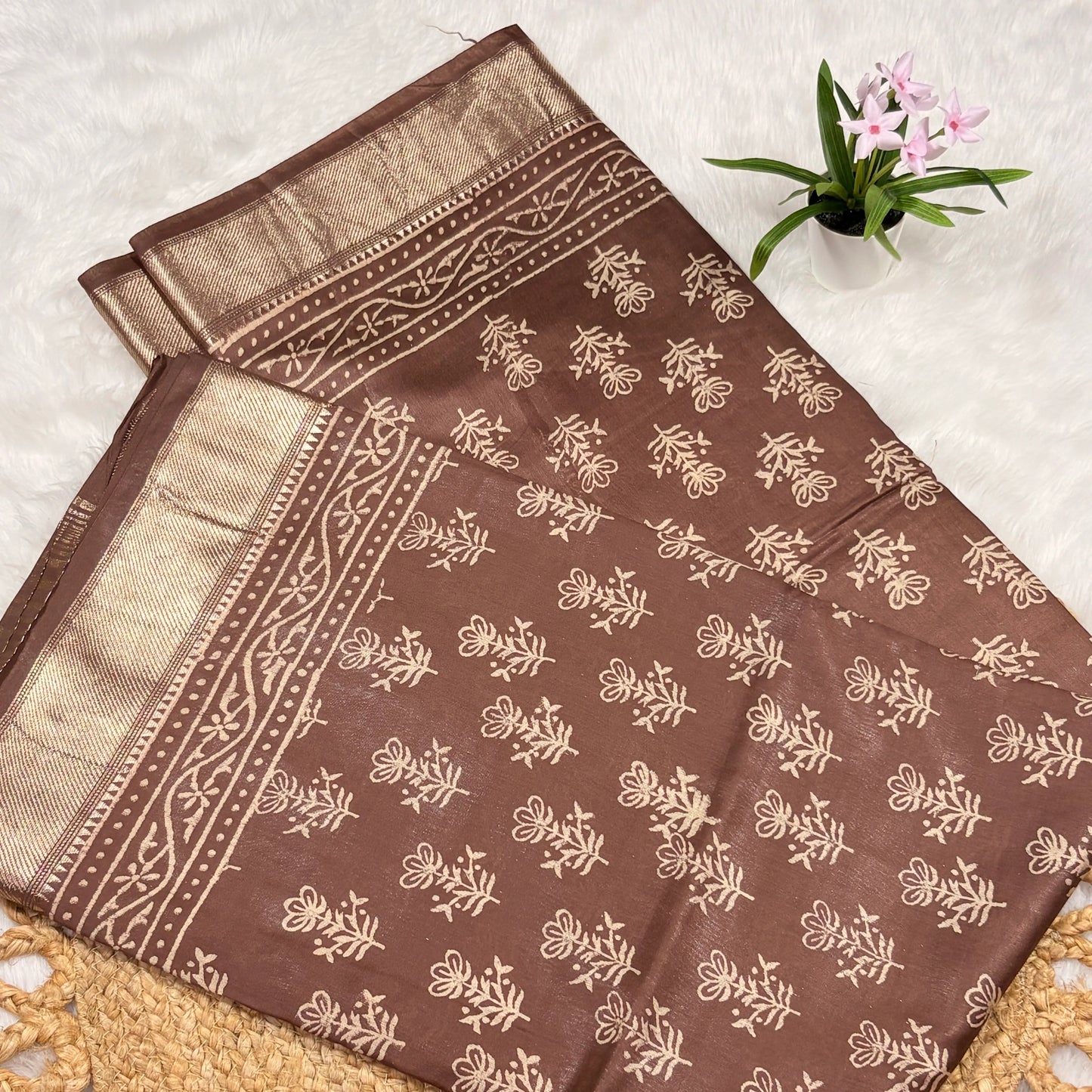 Brown fabric with beige floral patterns on a textured surface with a small plant.