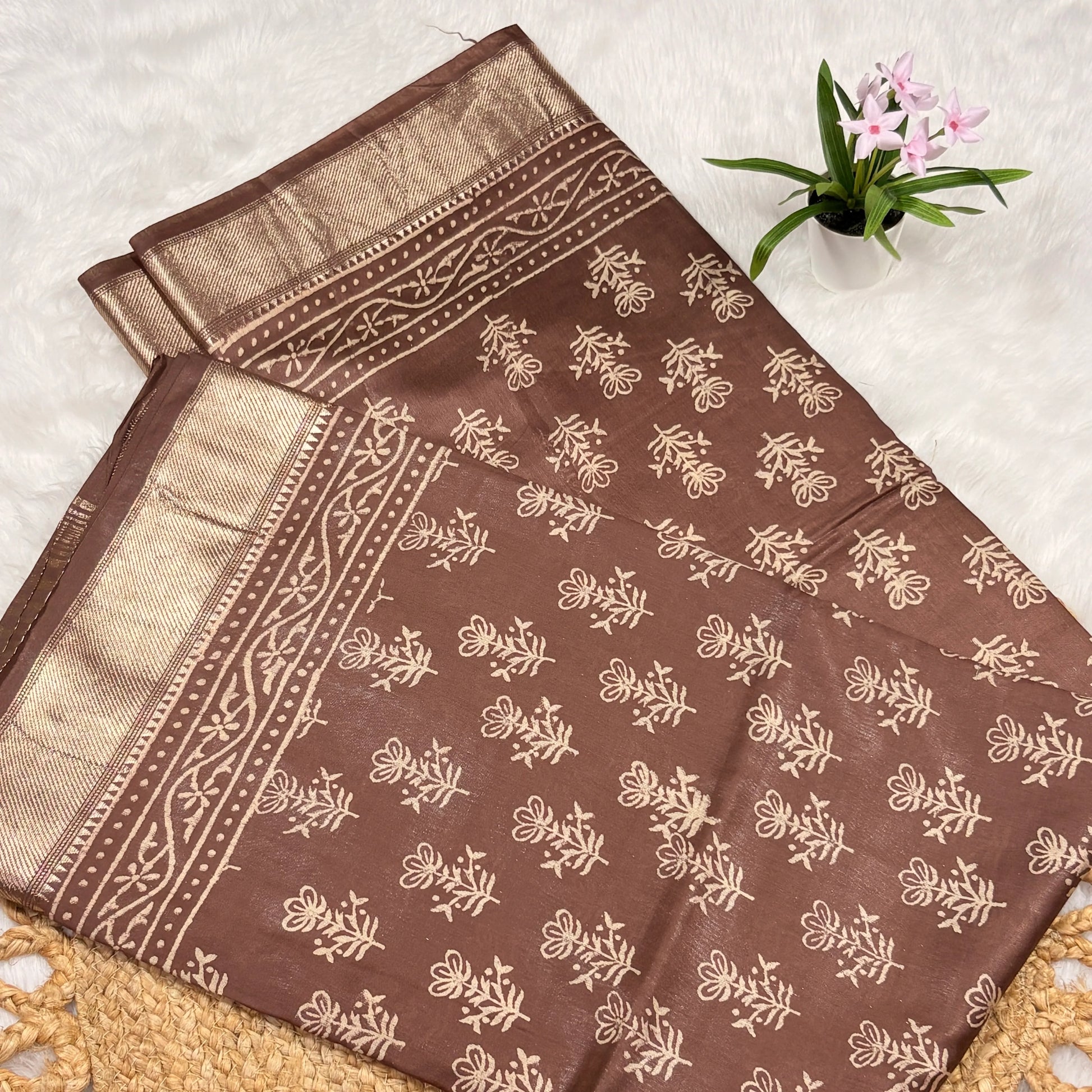 Brown fabric with beige floral patterns on a textured surface with a small plant.