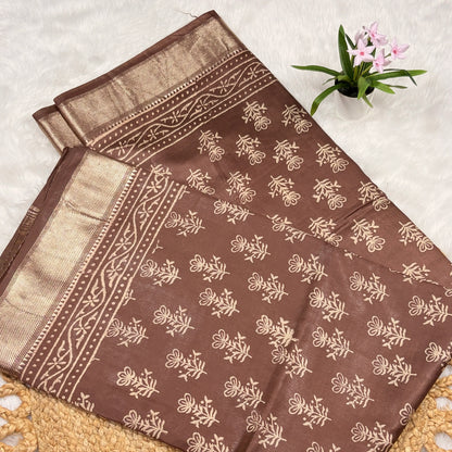 Brown fabric with beige floral patterns on a textured surface with a small plant.
