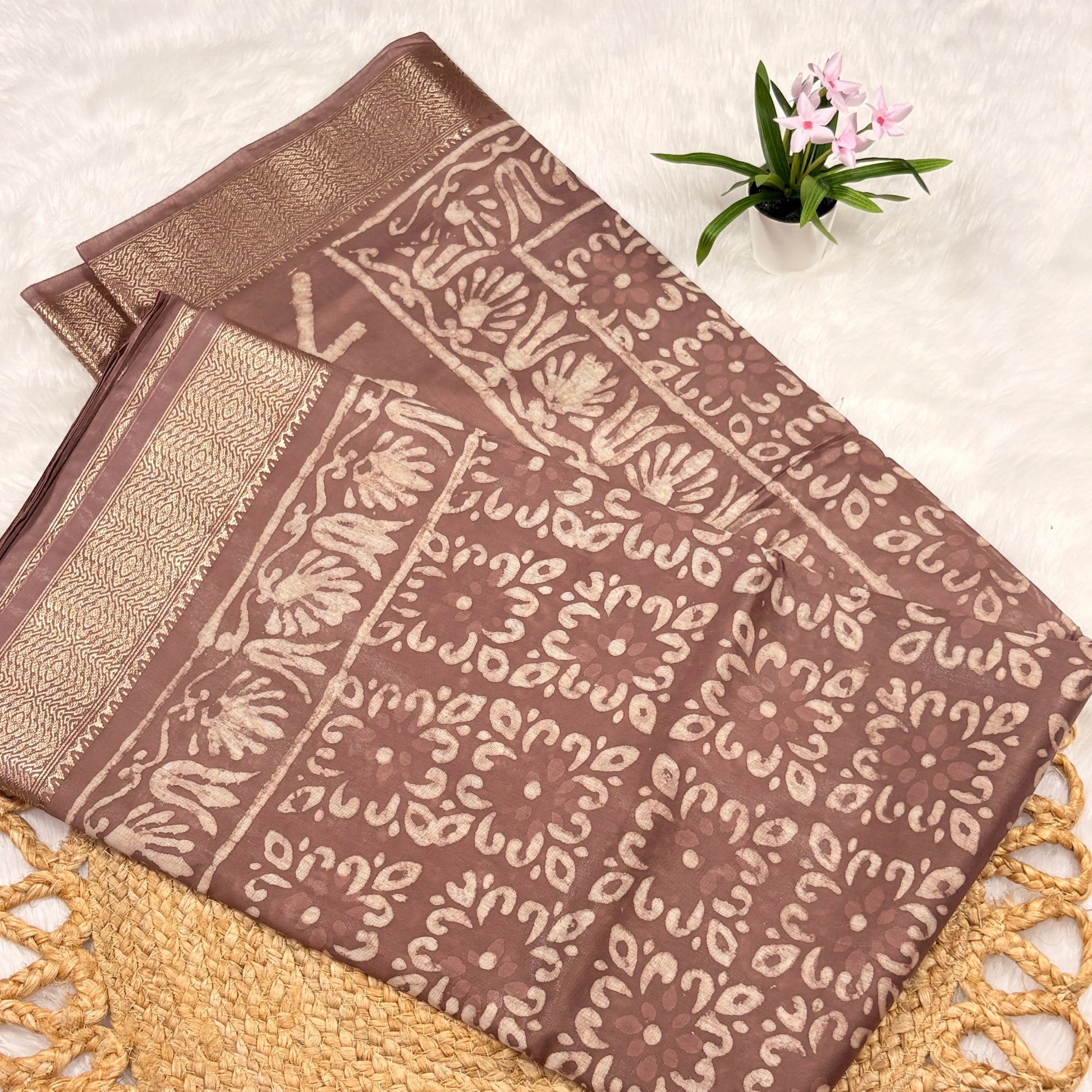 Brown fabric with intricate patterns on a textured surface with a small plant.