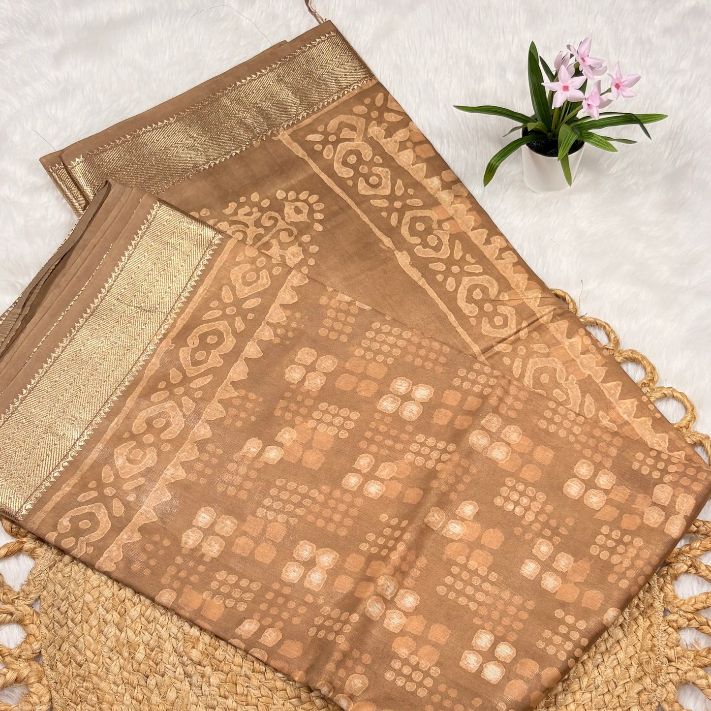 Brown fabric with intricate patterns on a textured surface with a small plant.