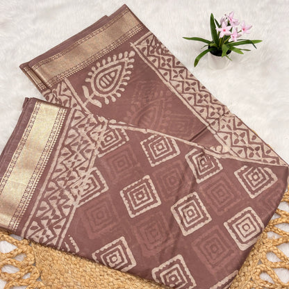 Brown fabric with geometric patterns on a textured surface with a small plant.