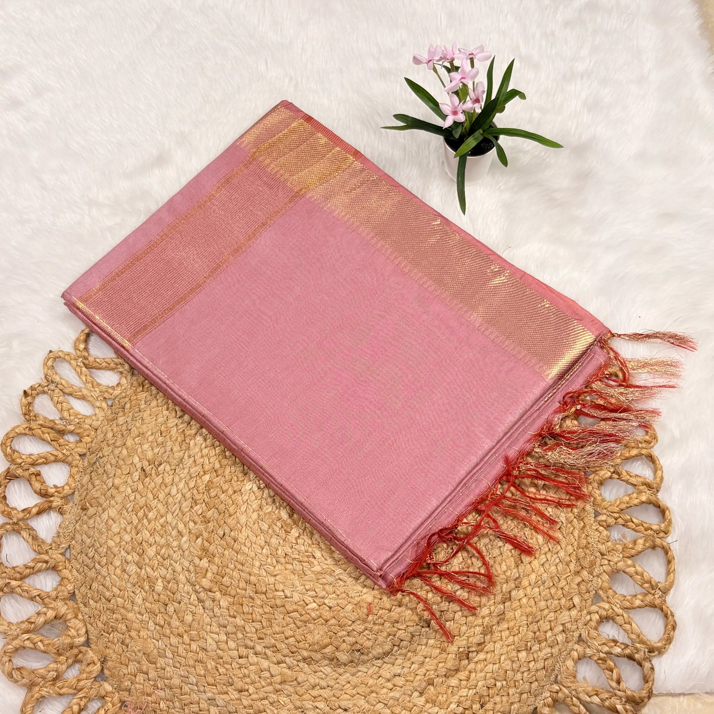 Pink saree with gold border and red fringes on a textured surface