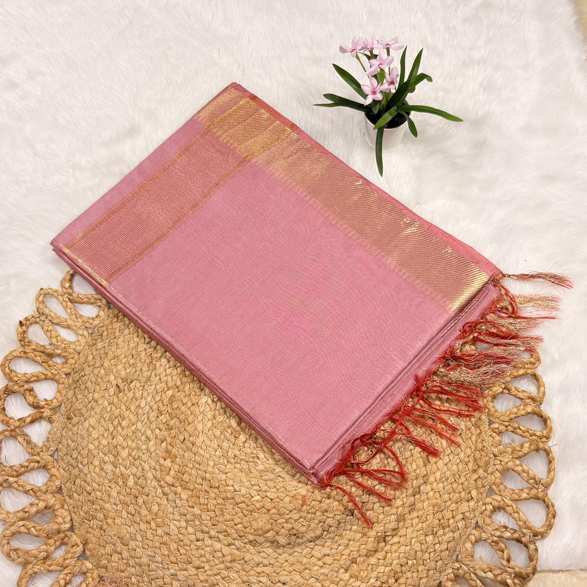 Pink saree with gold border and red fringes on a textured surface