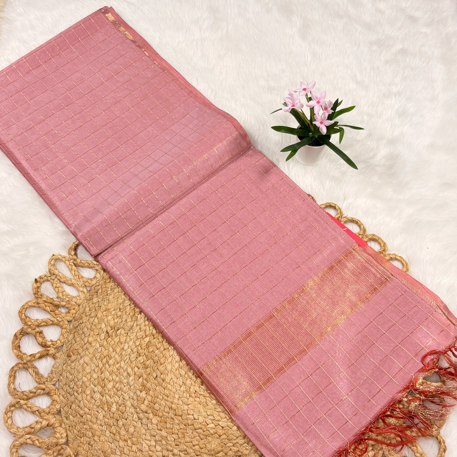 Pink woven mat with gold accents on a textured surface with a small plant.