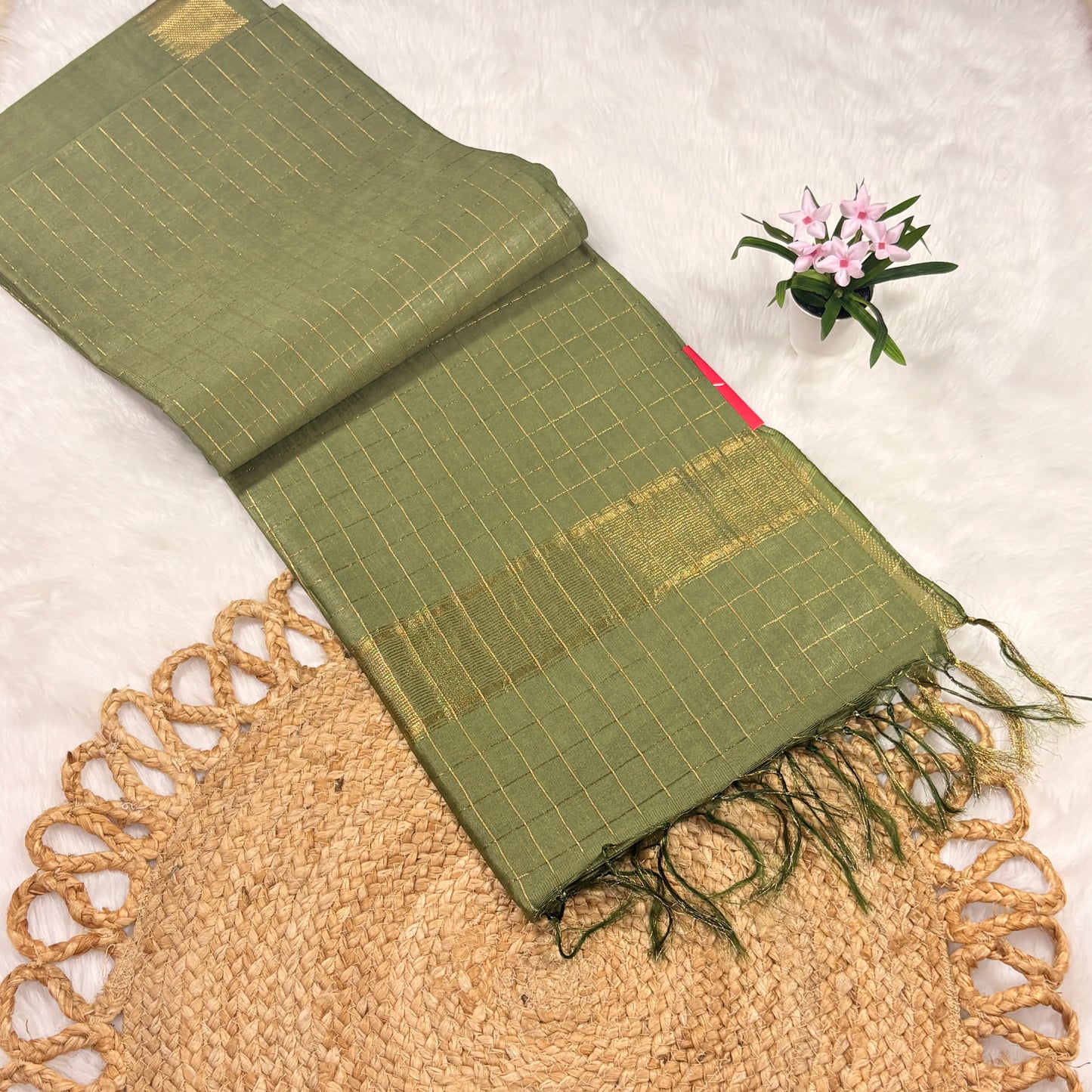 Green scarf with gold patterns on a textured surface with a small plant.