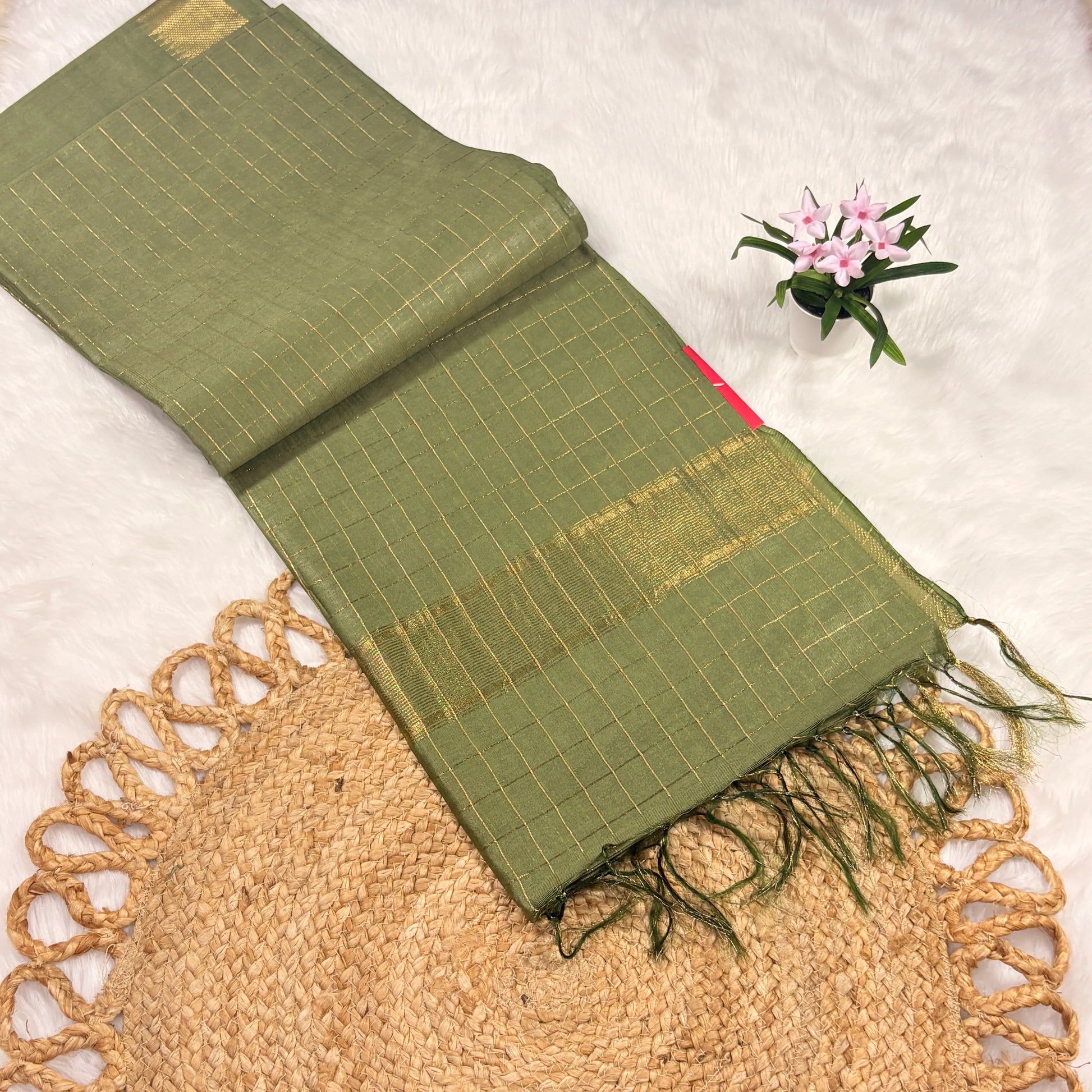 Green scarf with gold patterns on a textured surface with a small plant.