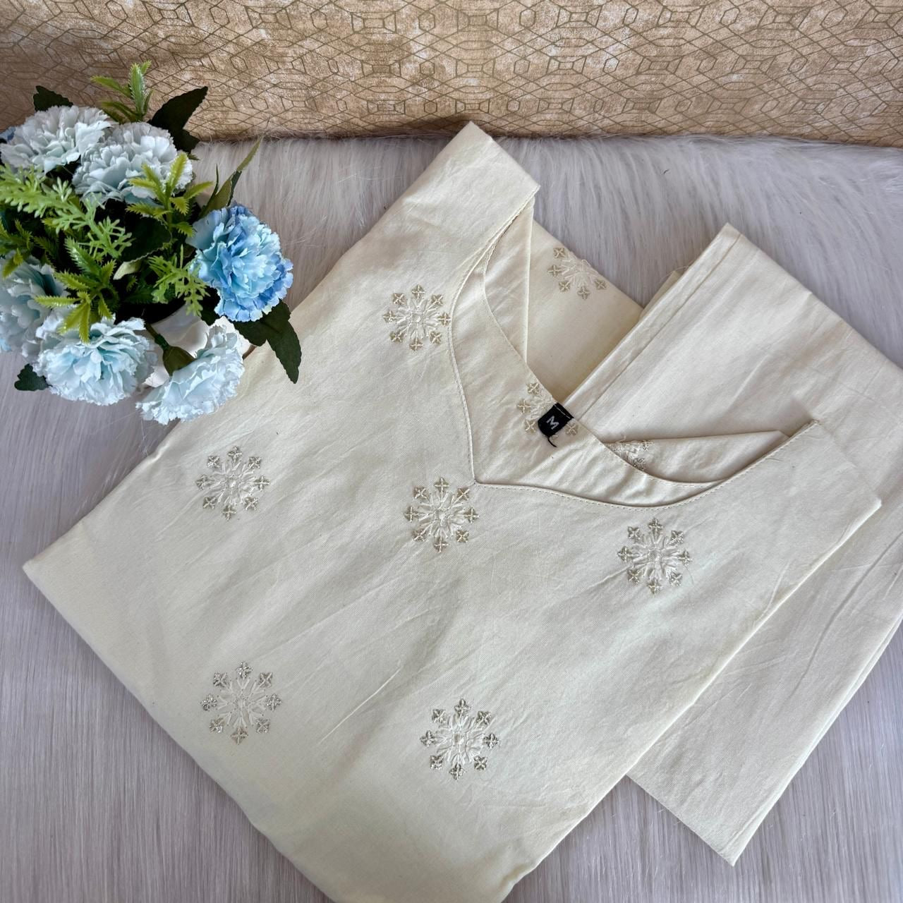 Beige embroidered blouse with floral arrangement on a textured surface