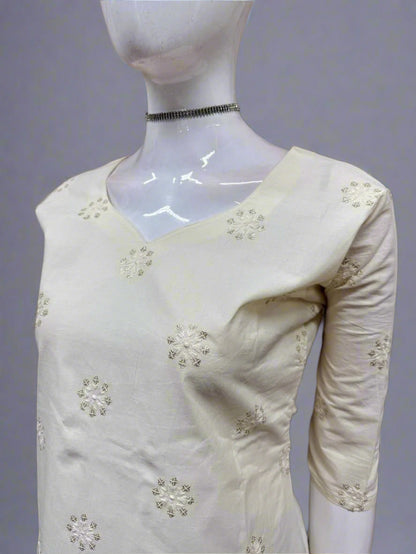 White dress with floral embellishments on a mannequin against a geometric-patterned wall.