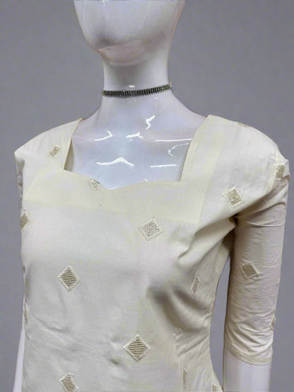 White saree with gold patterns on a mannequin against a geometric patterned wall.