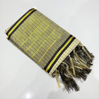 Kerala tissue silk saree neatly folded showing gold and black check weave body with yellow zari accents, bold black and gold stripe border, and dramatic black and gold mixed tassel fringe pallu – premium festive saree