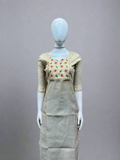 Mannequin wearing a beige dress with floral embroidery against a geometric patterned wall.
