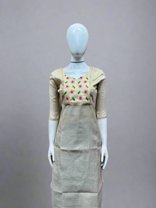 Mannequin wearing a beige dress with floral embroidery against a geometric patterned wall.