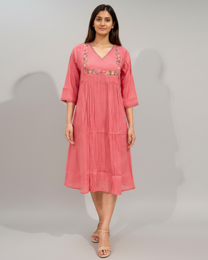 Woman wearing a pink dress with floral embroidery on a gray background