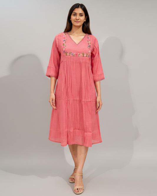 Woman wearing a pink dress with floral embroidery on a gray background