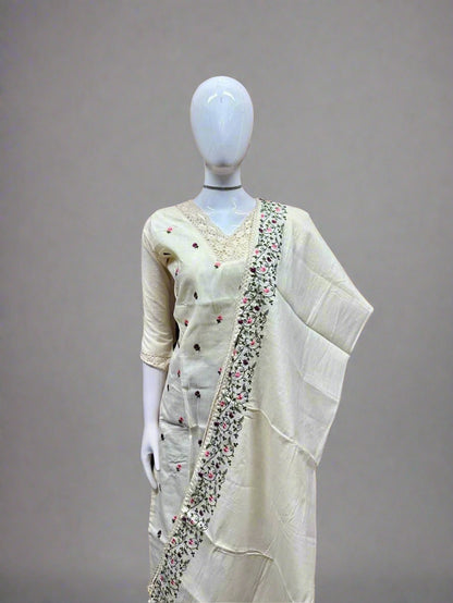 Mannequin wearing a cream saree with intricate patterns against a geometric patterned wall.