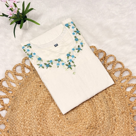 White blouse with floral embroidery on a textured surface with a plant in the background