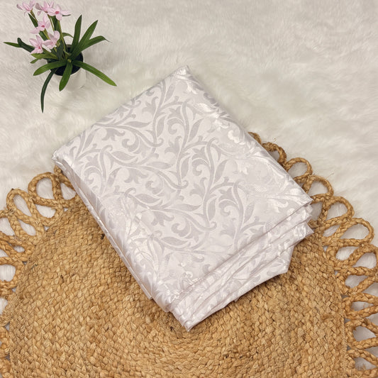 White patterned fabric on a textured surface with a plant in the corner