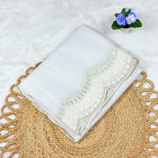 White embroidered fabric on a textured surface with a small potted plant in the background